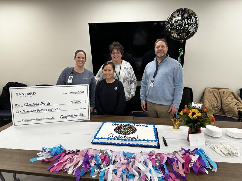 Three medical workers and a student display a giant check, cake and balloon.