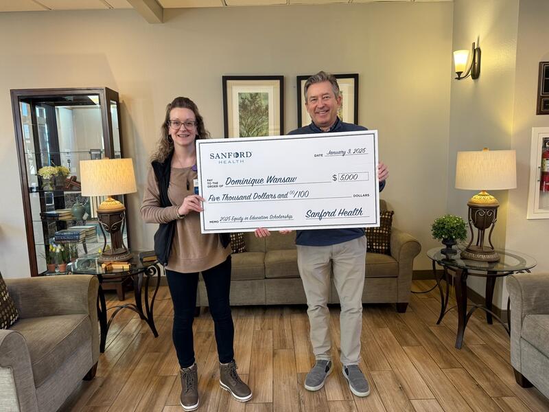 A woman and man hold a giant check in a senior living lobby.