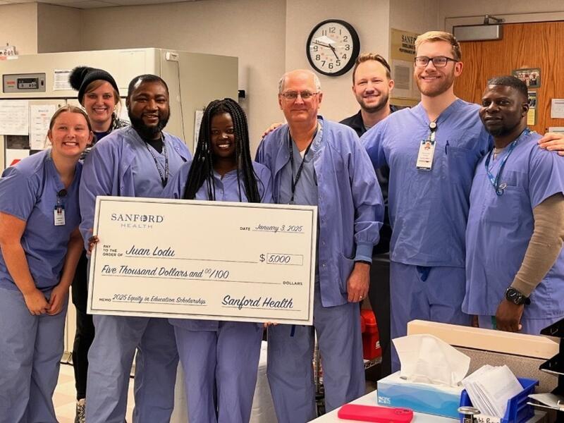 A diverse group of workers in scrubs smile and hold a giant check.