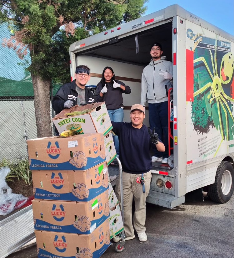 Four students standing at back of U-Haul truck with boxes of produce.