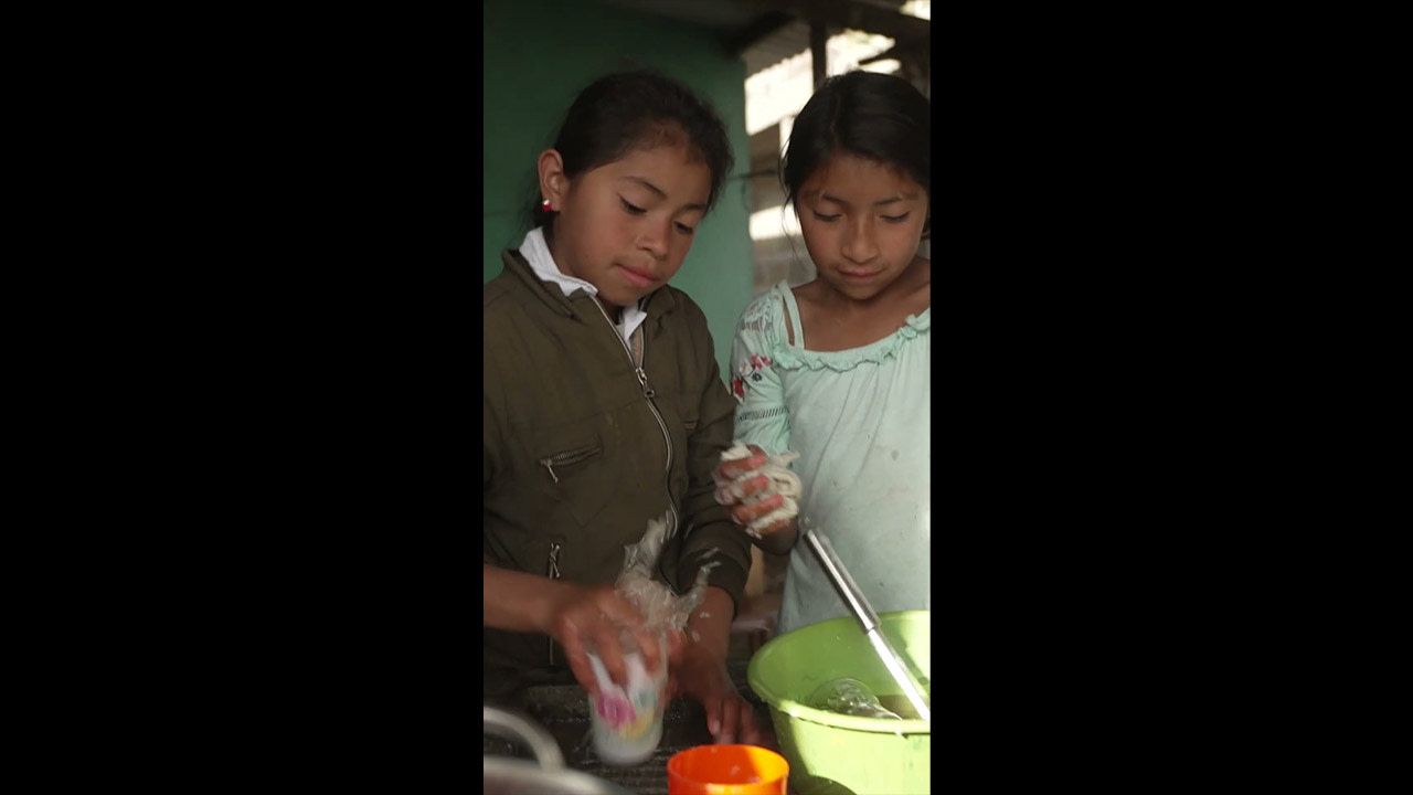 Two young Indian girls participating in a water purification process, using P&G CSDW packets to filter and clean water.