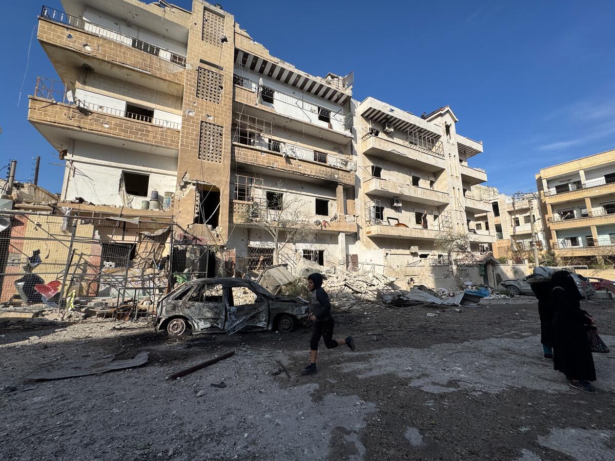 Silhouette of a child running over rubble, with light revealing the bombed-out remains of a building in the background.